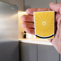 Rechteckiger Keramik-Kühlschrankmagnet (7x5 cm) in warmem Gelb. Gezeigt wird ein minimalistisches Fahrradrad mit feinen weißen Speichen, einem schwarzen Reifen am unteren Rand und einer winzigen menschlichen Silhouette im spürbaren 3D-Relief.