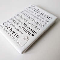 Rechteckiger Keramik-Kühlschrankmagnet (7x5 cm) mit seidenmatter Glasur. Auf hellem Grund steht der schwarze Spruch 'Zuhause ist wo die Liebe wohnt...' neben einer kleinen Haus-Illustration mit Herz im spürbaren 3D-Relief.