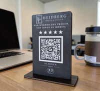 Personalisierter Holzaufsteller aus 4mm Holz mit eingraviertem Logo, Wunschtext „Wir würden uns freuen, von Ihnen zu hören!“, fünf Sternen, QR-Code mit Google-Logo und NFC-Symbol auf schwarzem Standfuß.