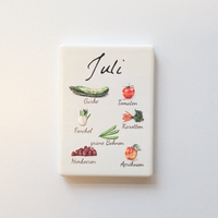 Saisonkalender Kühlschrankmagneten aus Keramik. Jeder Magnet repräsentiert einen Monat von Januar bis Dezember mit deutscher Beschriftung in geschwungener Schrift. Auf der cremefarbenen Oberfläche sind detailreiche, farbige Illustrationen von saisonalem Obst und Gemüse mit den jeweiligen Namen abgebildet.