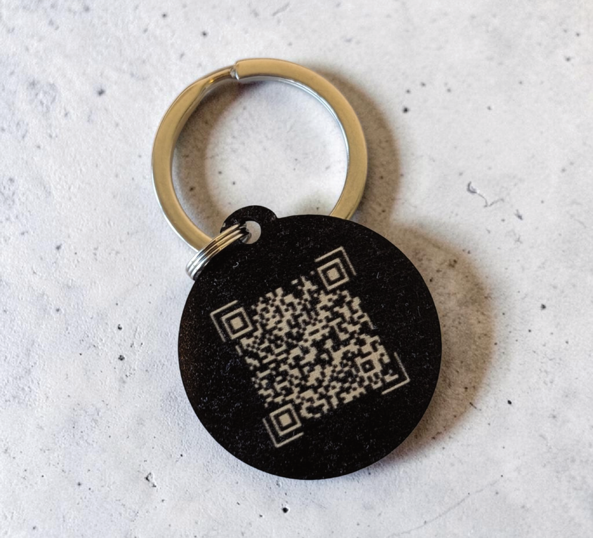 Hand hält einen runden, schwarzen NFC-Schlüsselanhänger aus Holz mit der
Aufschrift "DEIN LOGO -oder- NAME". Im Hintergrund eine kleine grüne Pflanze
auf hellem Tisch.