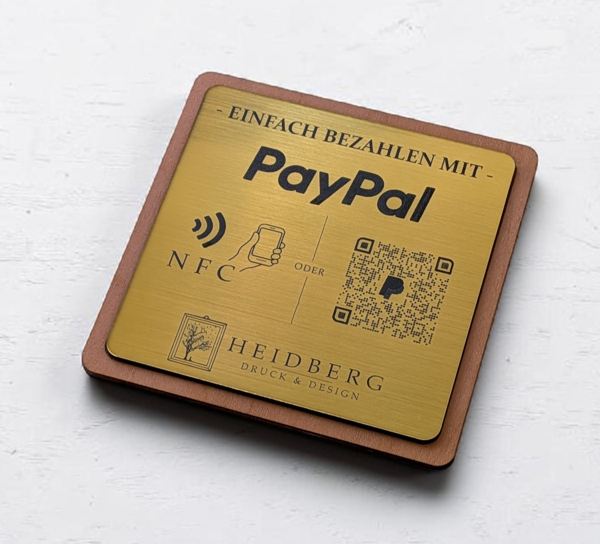 Quadratischer PayPal-Tischaufsteller aus dunklem Holz mit einer gravierten, gold gebürsteten Kunststoffplatte. Auf der Platte sind ein QR-Code, ein NFC-Symbol und das PayPal-Logo zu sehen, perfekt geeignet für kontaktlose Zahlungen auf einer Ladentheke.