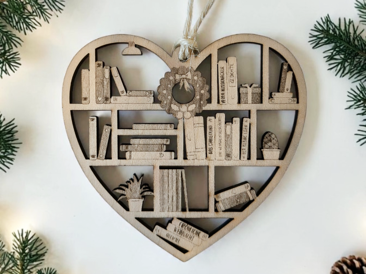 Herzförmiger Weihnachtsbaum-Anhänger aus hellem Holz im Bücherregal-Design mit gravierten Büchern, kleinem Weihnachtskranz und Zimmerpflanzen an einer Kordel.