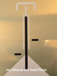 Minimalistische Bauhaus-Illustration eines Fahrrads in der Vorderansicht auf einer gebürsteten, gold-glänzenden Aluminiumplatte (Alu-Dibond). Das Design zeigt klare weiße und schwarze Linien vor einem edlen Metallhintergrund. Das Bild lehnt modern an einer weißen Wand zwischen zwei Zimmerpflanzen.
