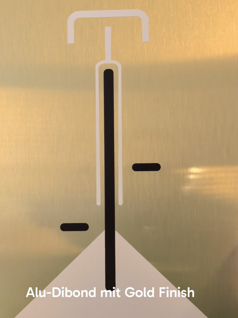 Minimalistische Bauhaus-Illustration eines Fahrrads in der Vorderansicht auf einer gebürsteten, gold-glänzenden Aluminiumplatte (Alu-Dibond). Das Design zeigt klare weiße und schwarze Linien vor einem edlen Metallhintergrund. Das Bild lehnt modern an einer weißen Wand zwischen zwei Zimmerpflanzen.